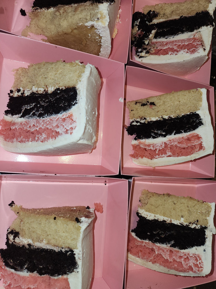 Slices of vanilla, chocolate and strawberry layer cake in pink boxes